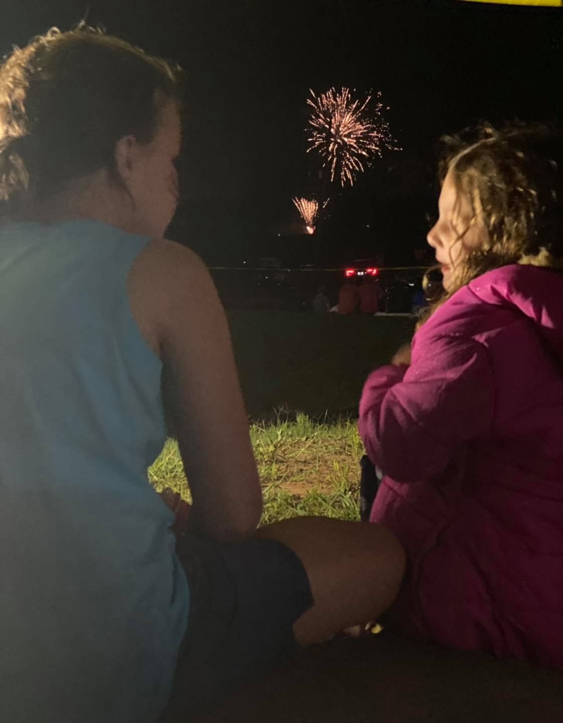 Two girls are sitting on the ground watching fireworks