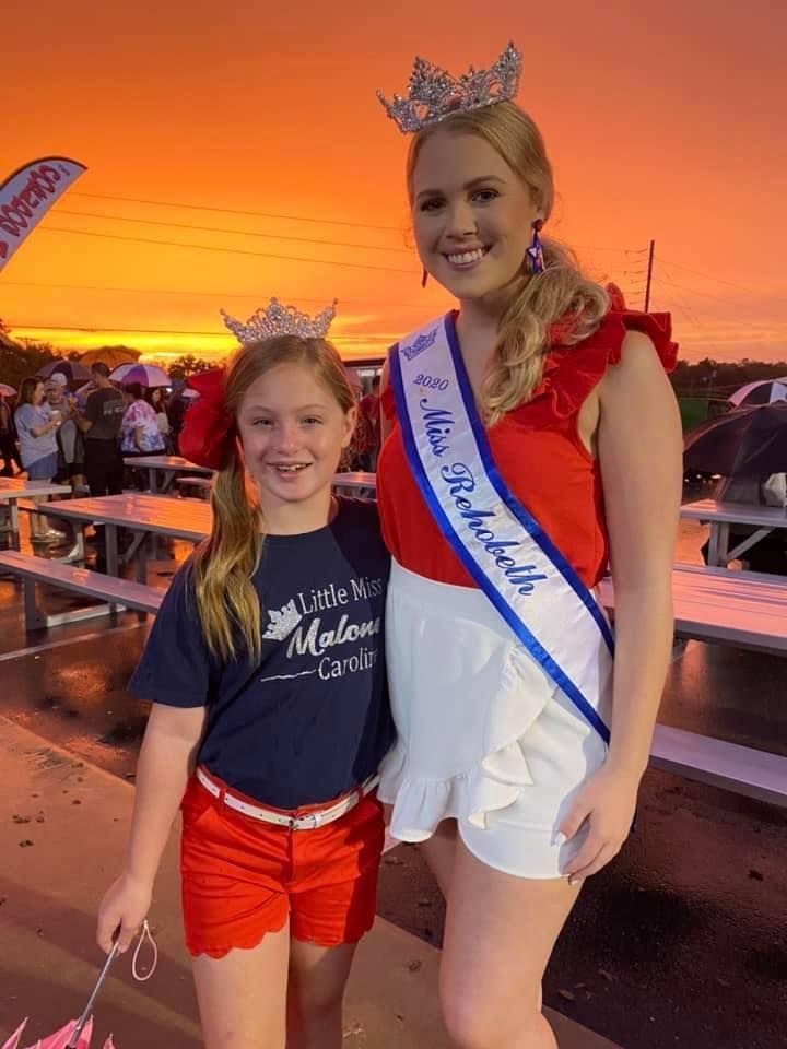 A woman in a crown and sash is standing next to a little girl.