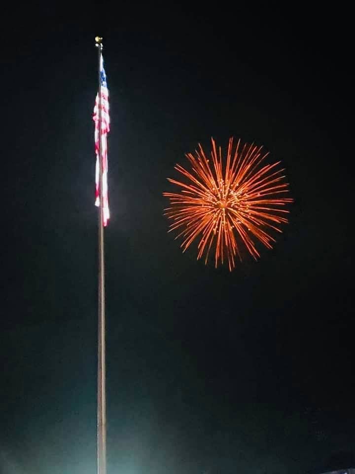 A fireworks display with an american flag in the foreground