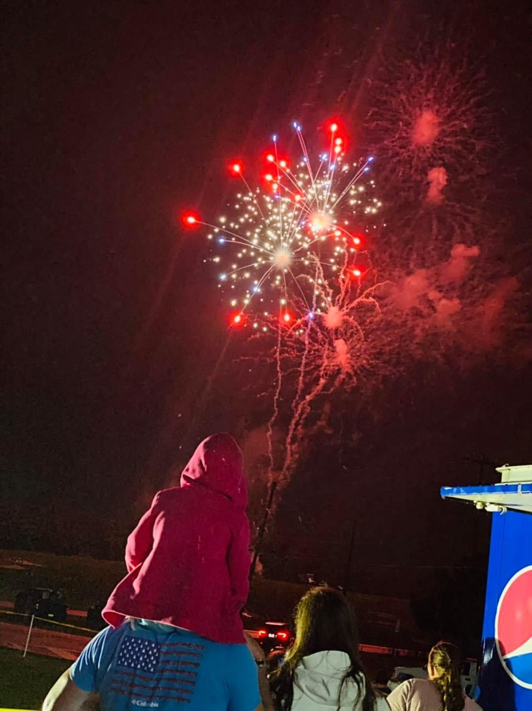 A man is carrying a child on his shoulders while watching fireworks.