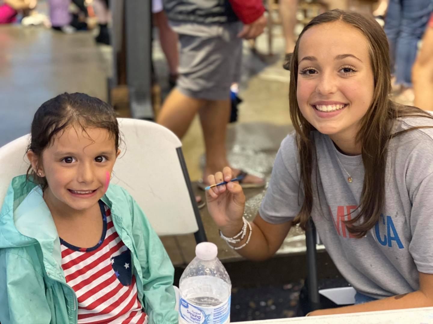 Two young girls are sitting at a table with a bottle of water.