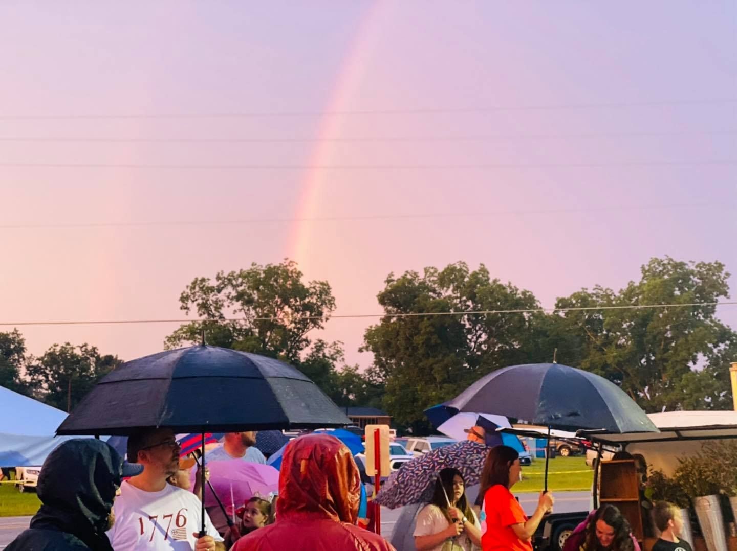 A group of people standing under umbrellas in front of a rainbow.