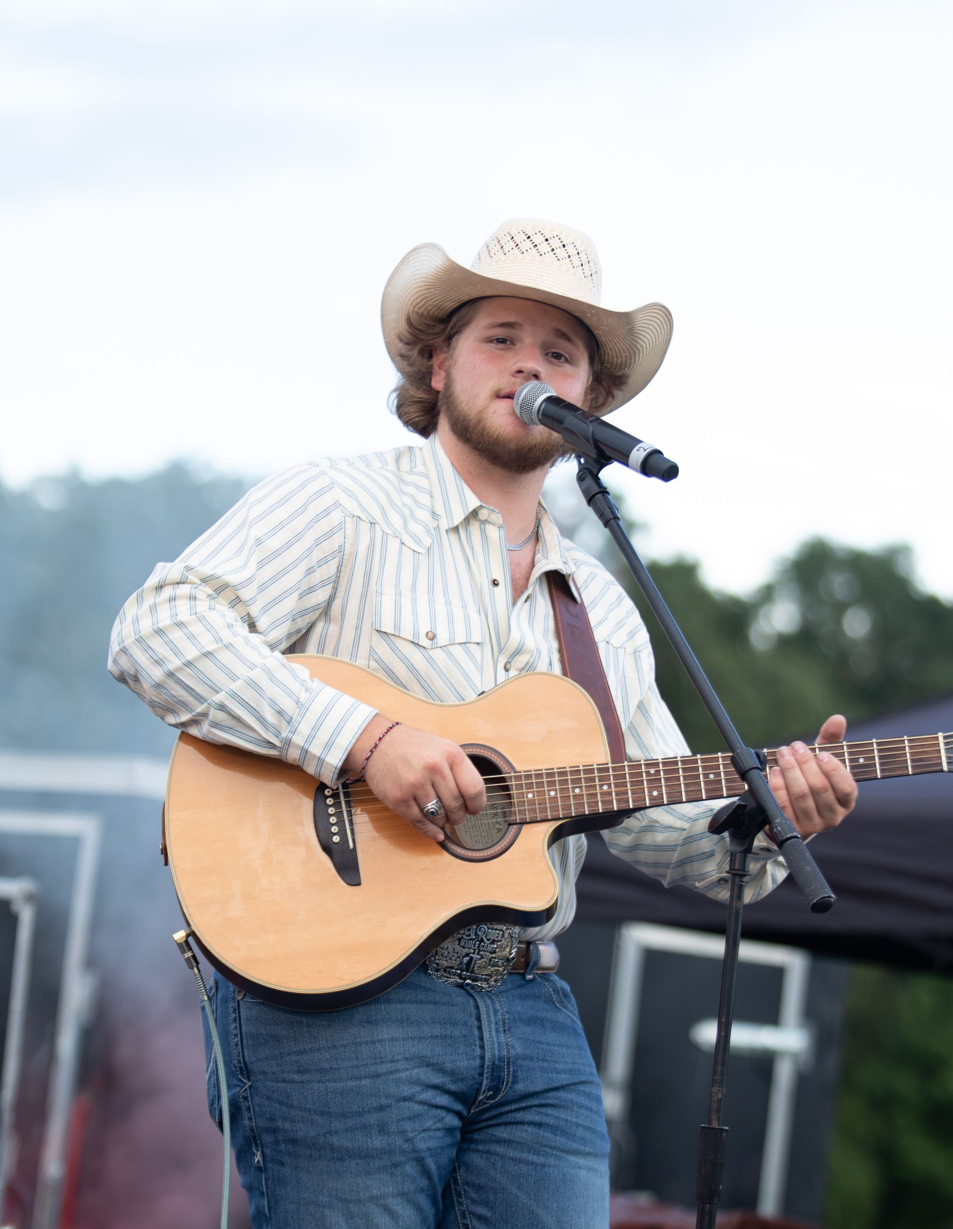Man in cowboy hat plays acoustic guitar and sings into microphone.