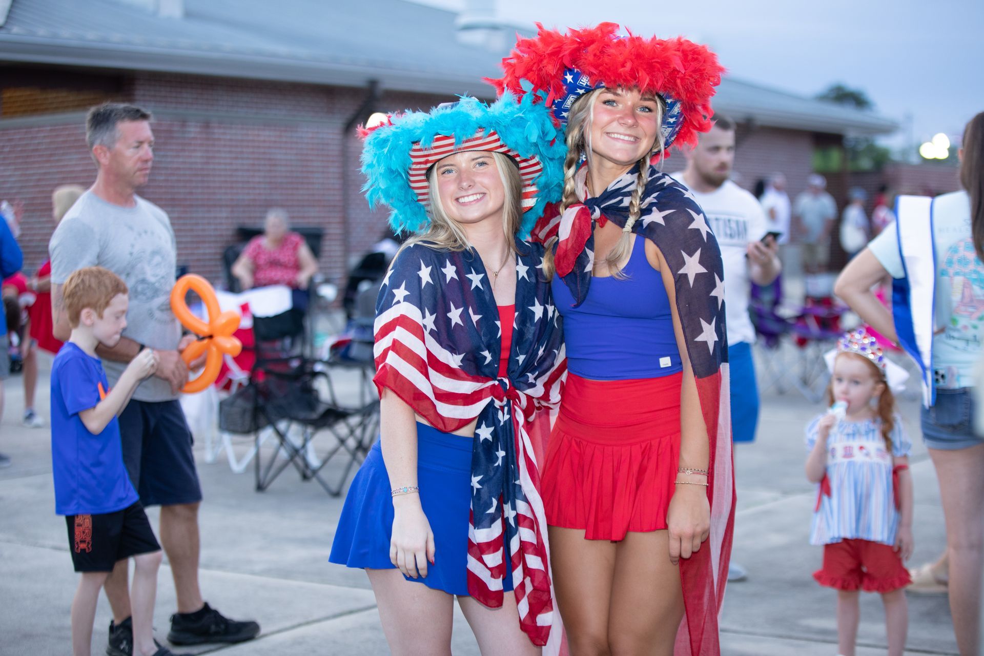 Two young women in patriotic outfits with festive hats at an outdoor gathering.