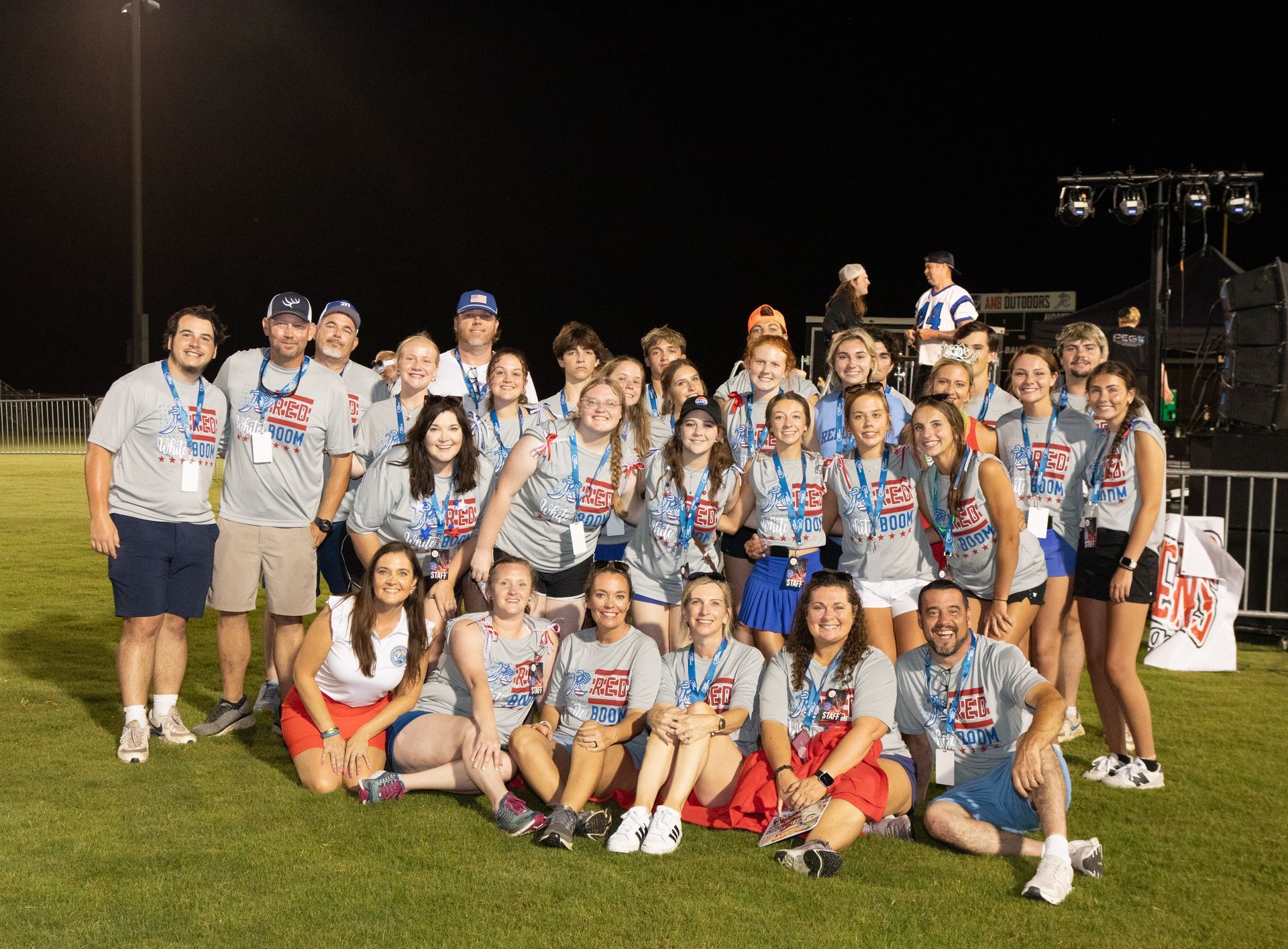 Group of people in matching shirts posing on a grassy field at night; some are kneeling.