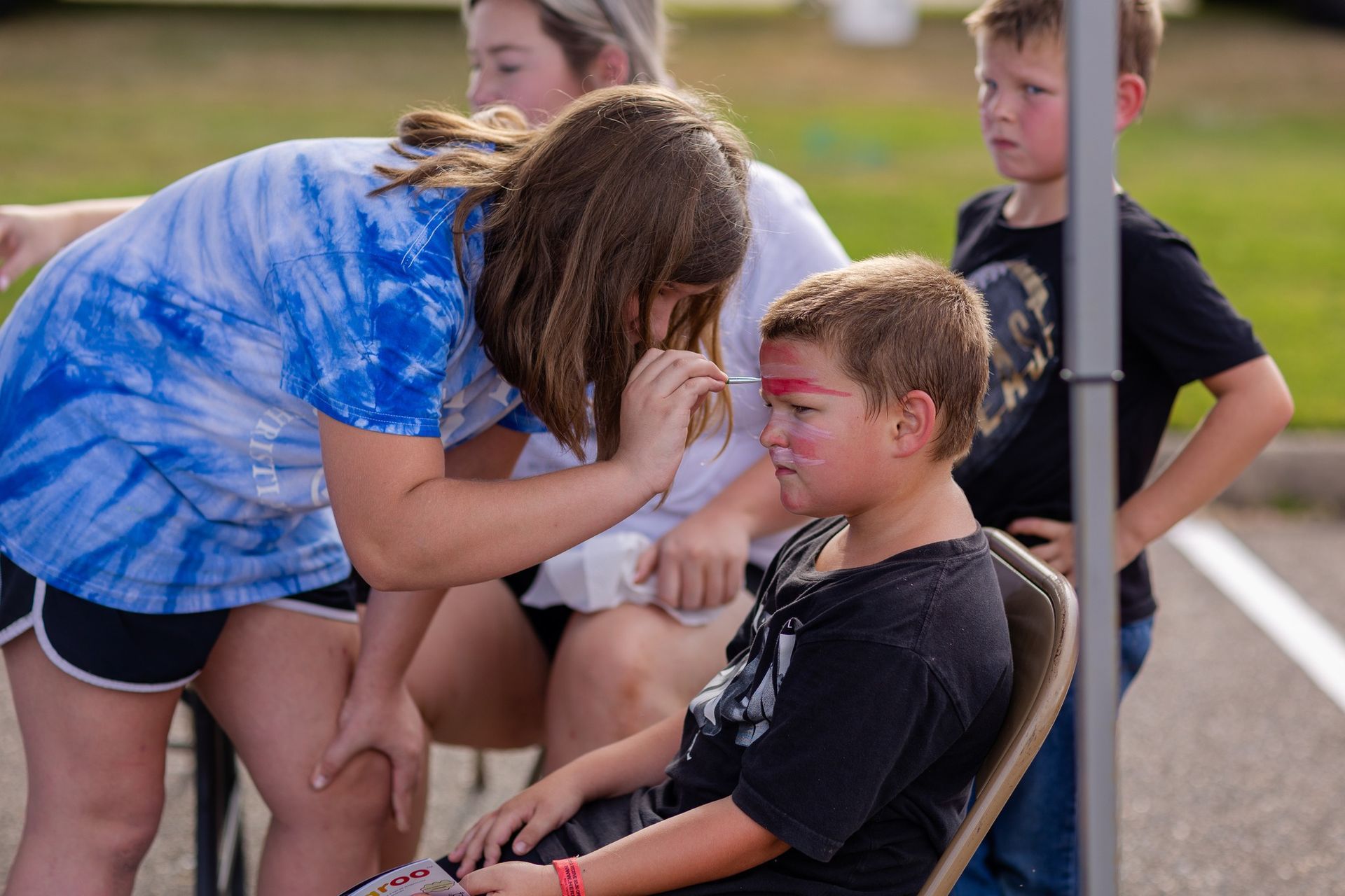 A girl is applying face paint to a boy 's face.