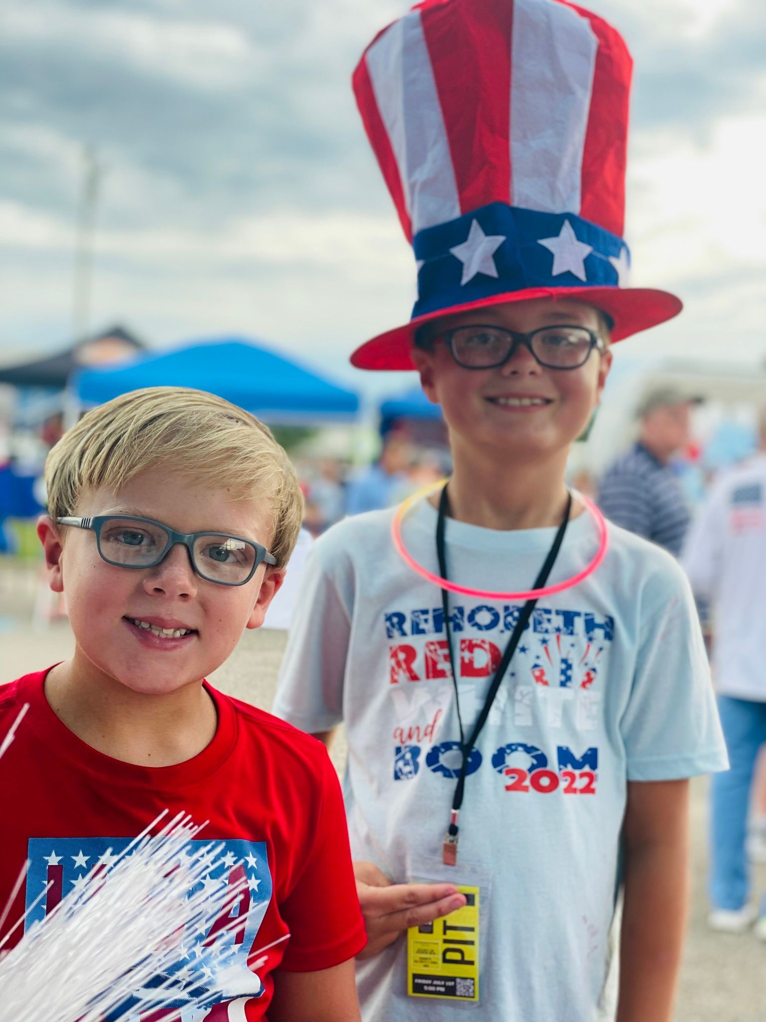 Two young boys wearing patriotic shirts and hats are posing for a picture