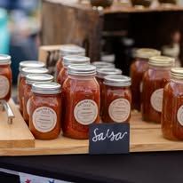 A bunch of jars of salsa are sitting on a wooden table.