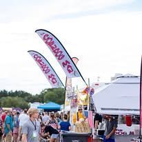 A group of people are standing around a food stand at a festival.