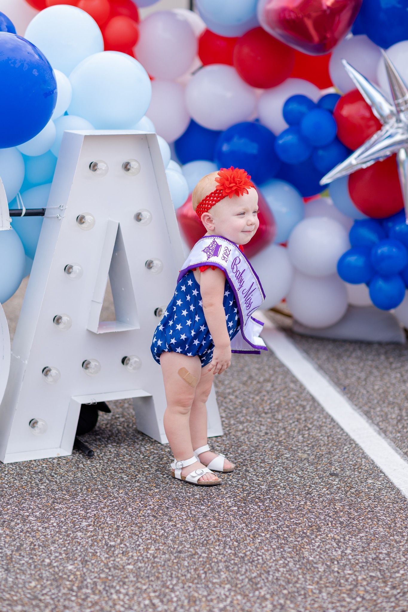 A little girl is standing in front of a large letter a surrounded by balloons.
