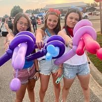 Three girls are standing next to each other holding balloons in their hands.