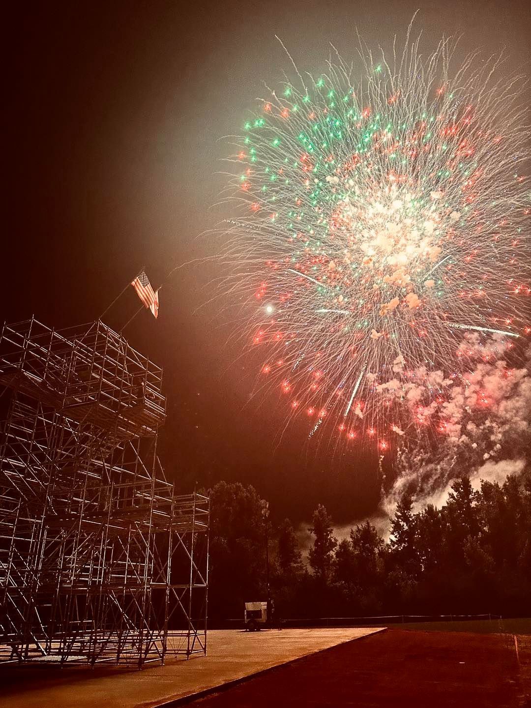 A large fireworks display is taking place in the night sky over a stadium.