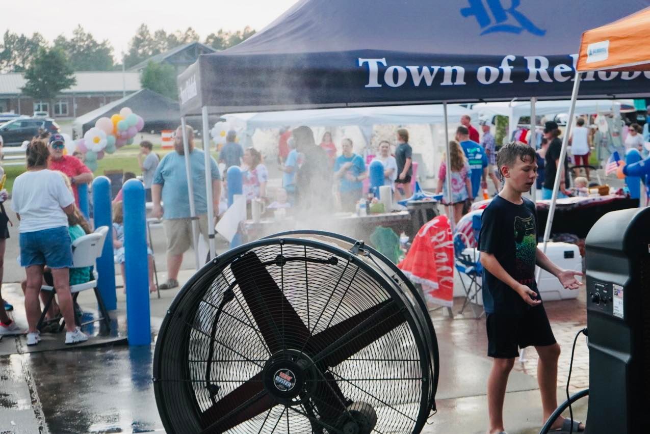 A boy stands in front of a large fan in front of a tent that says town of reno