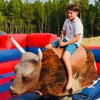 A young boy is riding a mechanical bull on a bouncy castle.