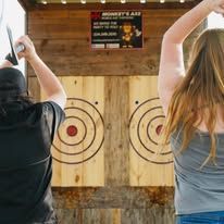 A man and a woman are standing in front of a wooden target holding axes.