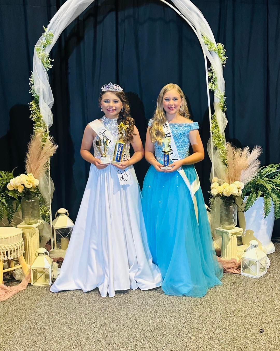 Two young girls in dresses are standing next to each other under an arch.