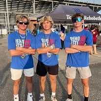 Three young men are standing next to each other in front of a tent.