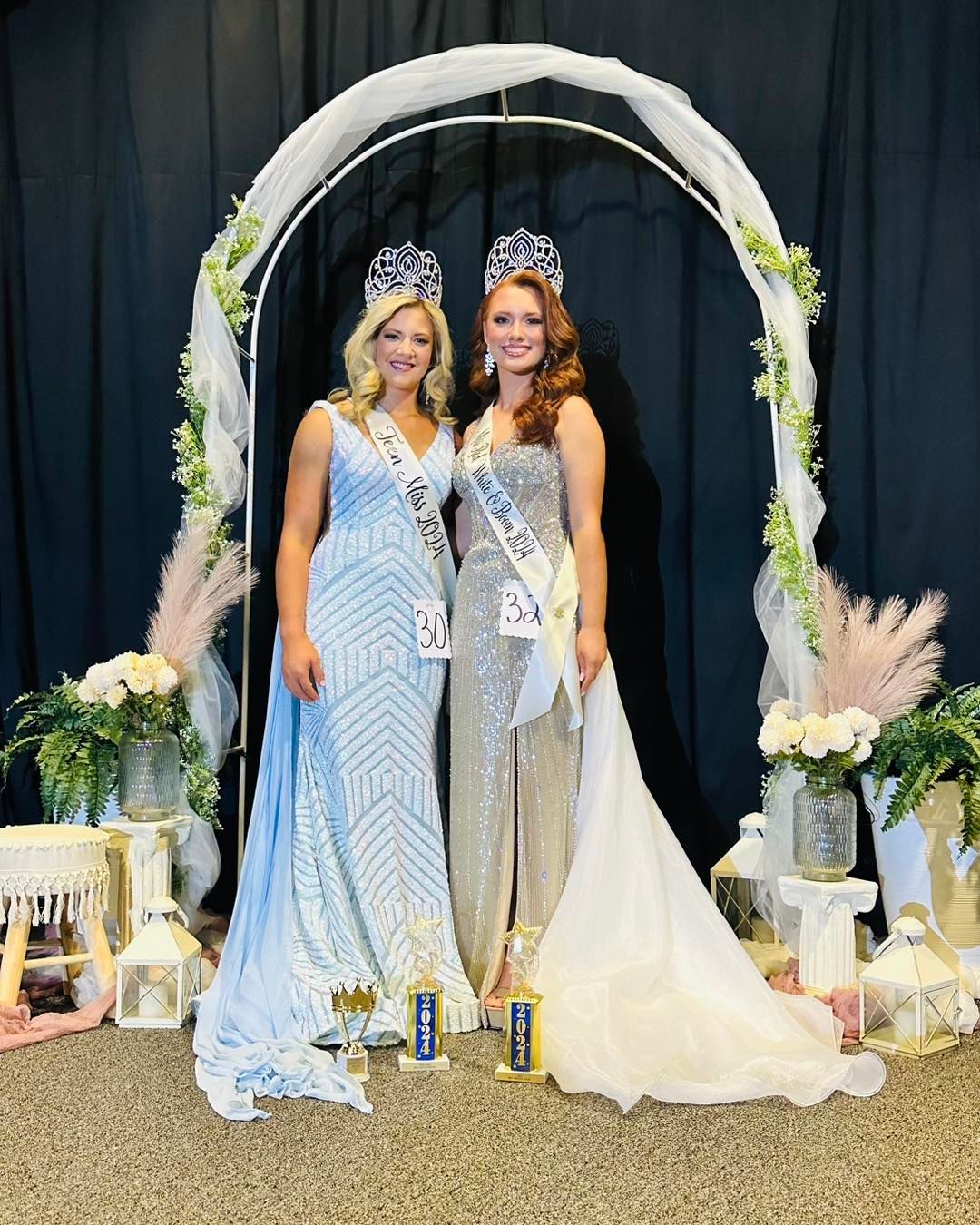 Two women are posing for a picture in front of a white arch.
