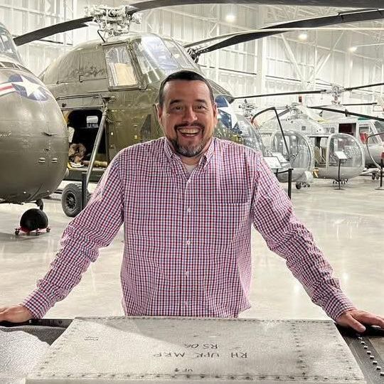 A man is standing in front of a helicopter in a hangar.