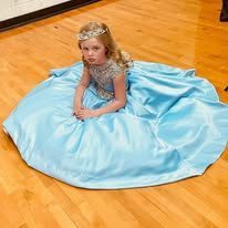 A little girl in a blue dress is sitting on the floor.