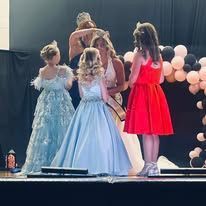 A group of girls in dresses are standing on a stage.