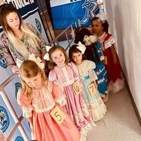 A group of young girls in dresses are standing next to each other in a hallway.