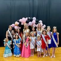 A group of young girls in dresses and sashes are posing for a picture.