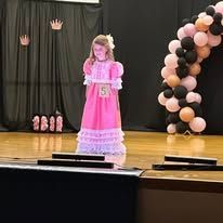 A little girl in a pink dress is standing on a stage.