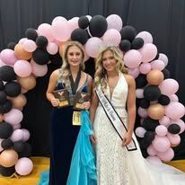 Two women are posing for a picture in front of a balloon arch.
