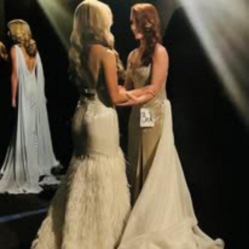 Two women in long dresses are standing next to each other on a stage.