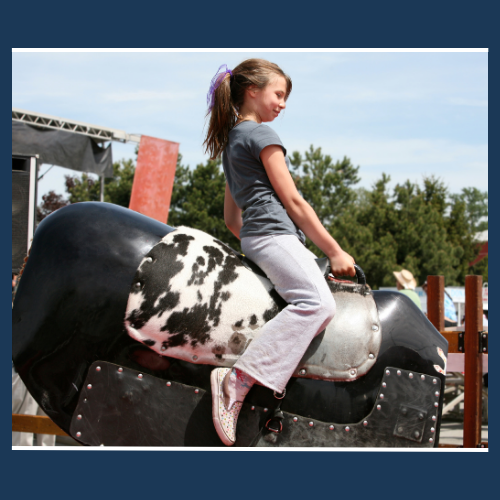 A little girl is riding a mechanical bull.