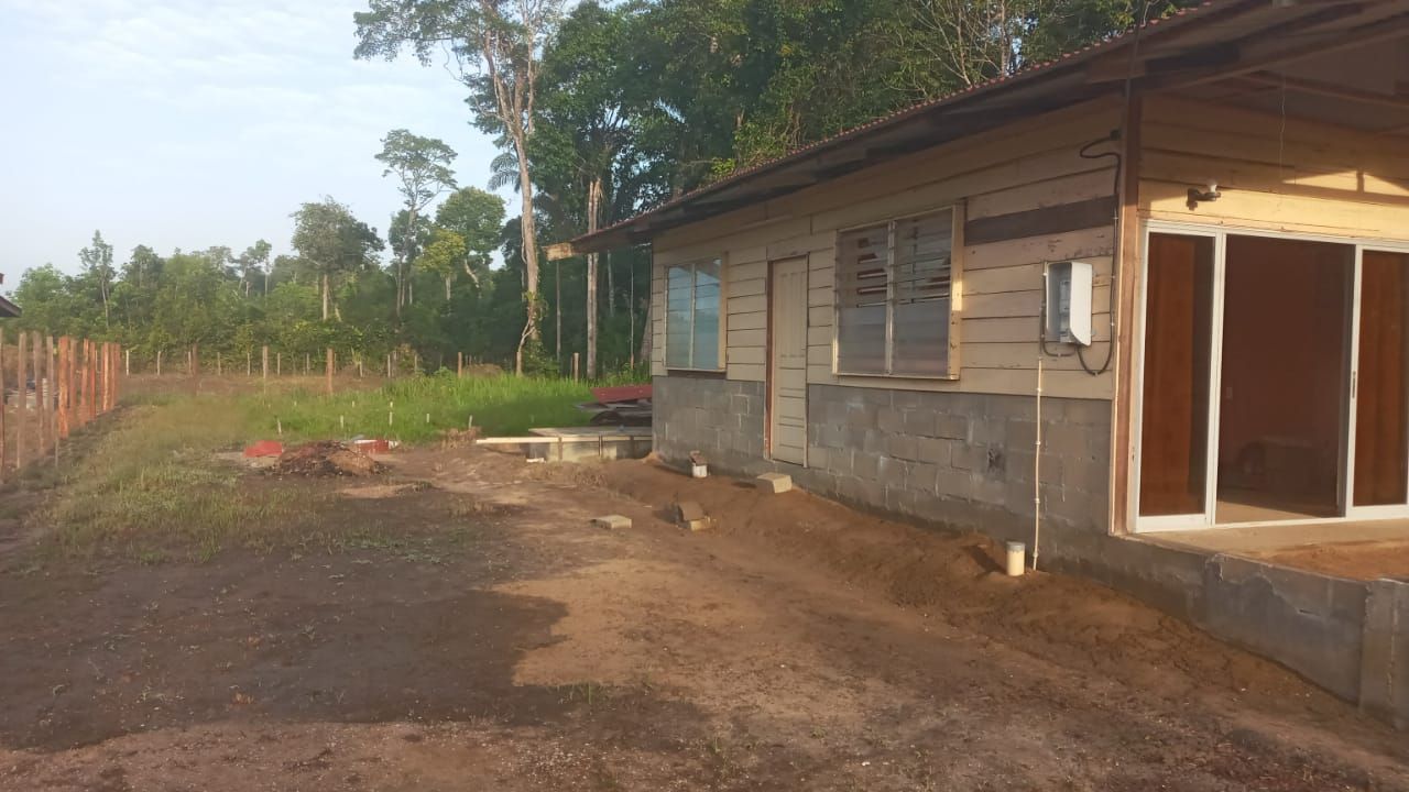 Wooden building with glass doors and windows in a rural setting, dirt path, and trees.