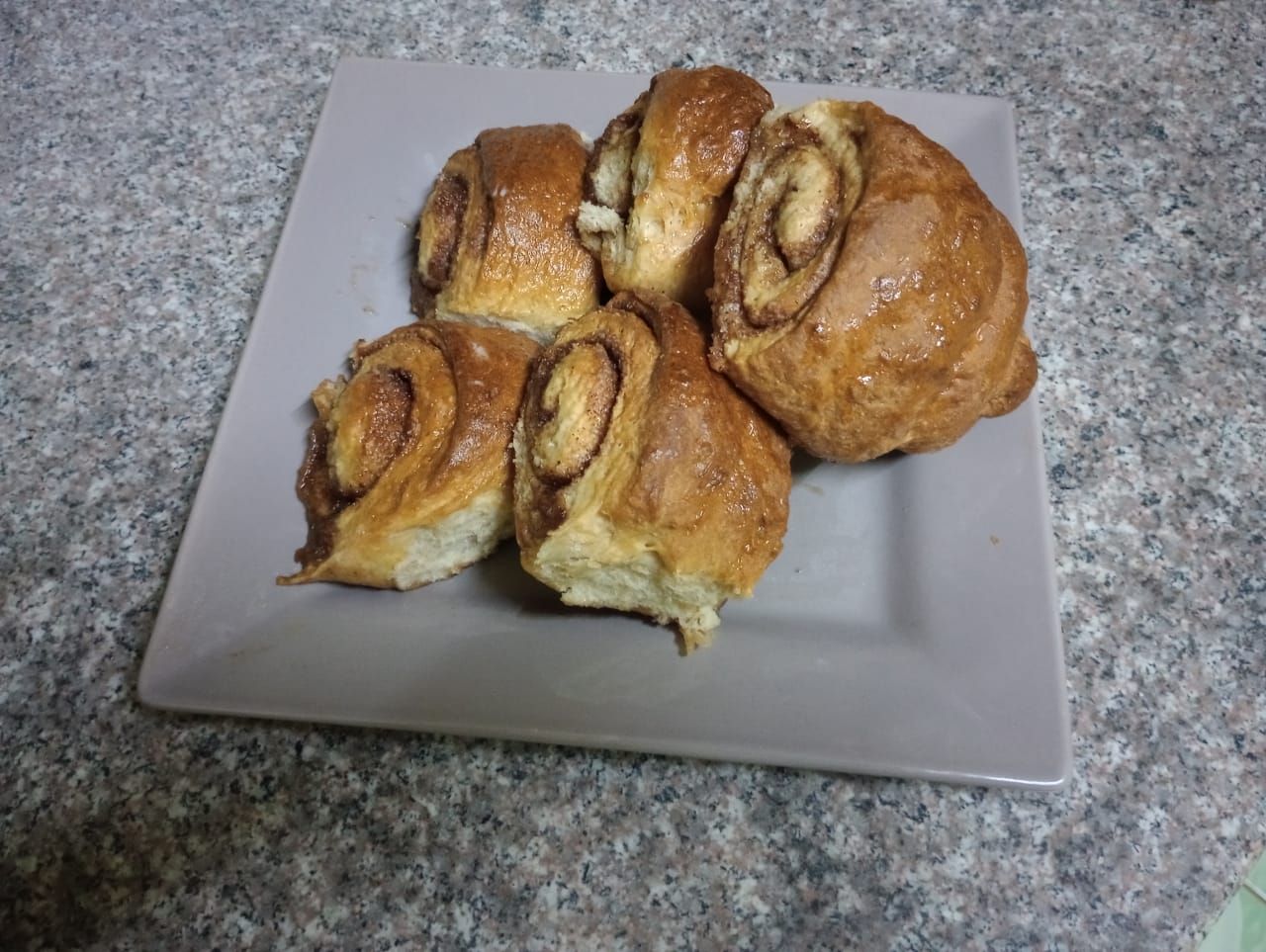 Cinnamon rolls on a gray square plate, placed on a granite countertop.