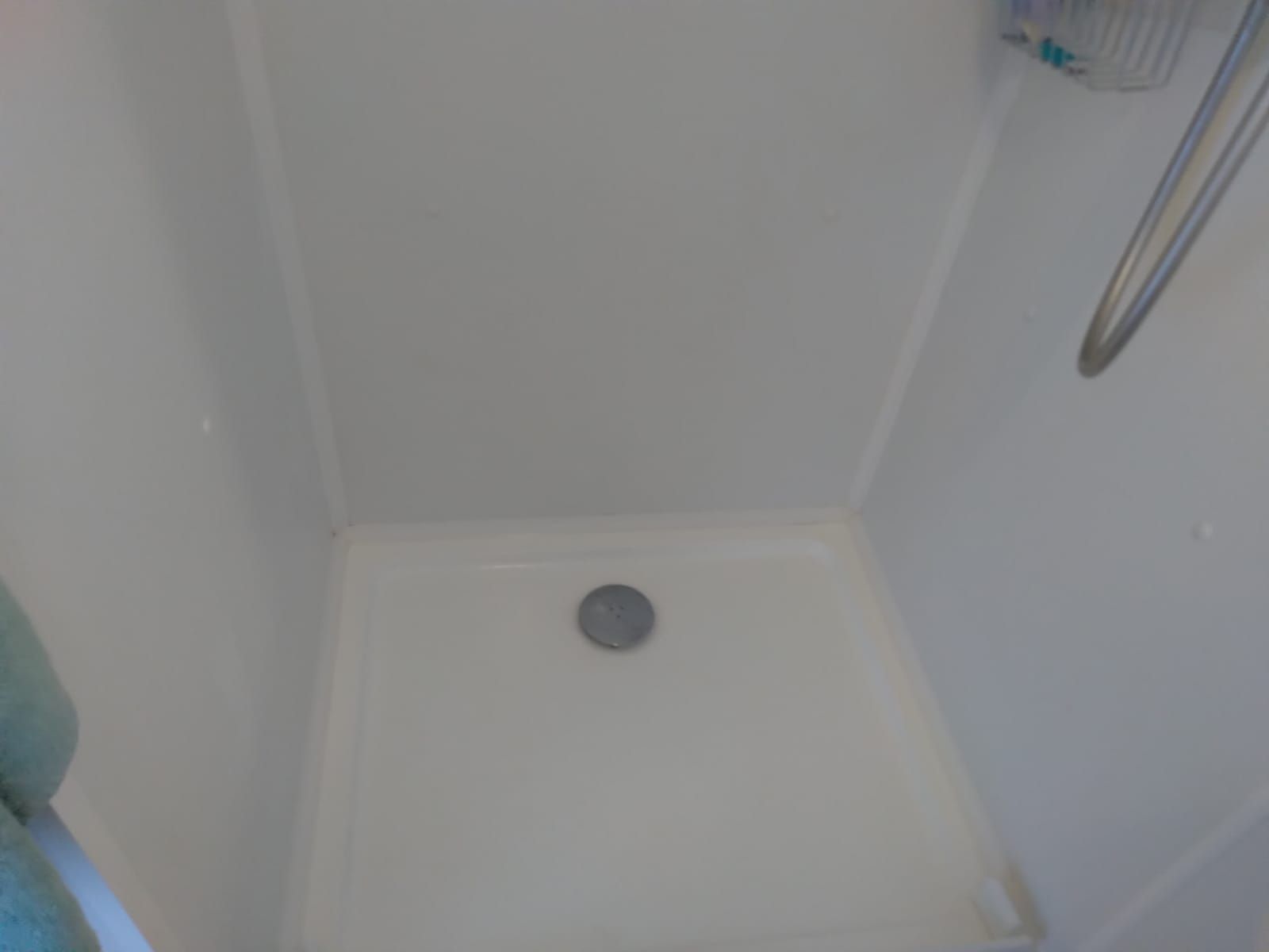 View inside a small, white shower stall with a drain in the center.
