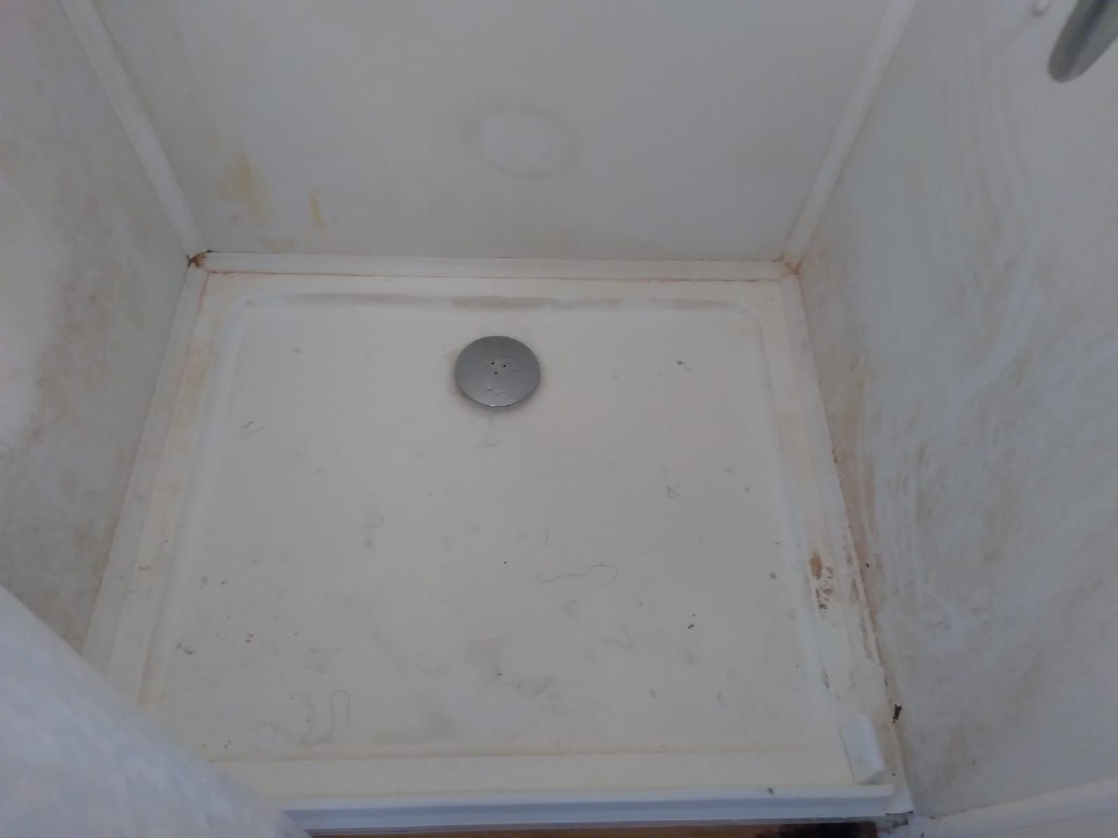 White, dirty shower stall with brown stains. Drain in the center.