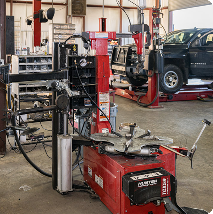 Auto repair shop with red tire-changing machine and a lifted SUV in the background
