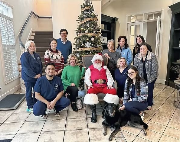 A group of people standing around Santa Claus and a dog in front of a decorated Christmas tree in a foyer.