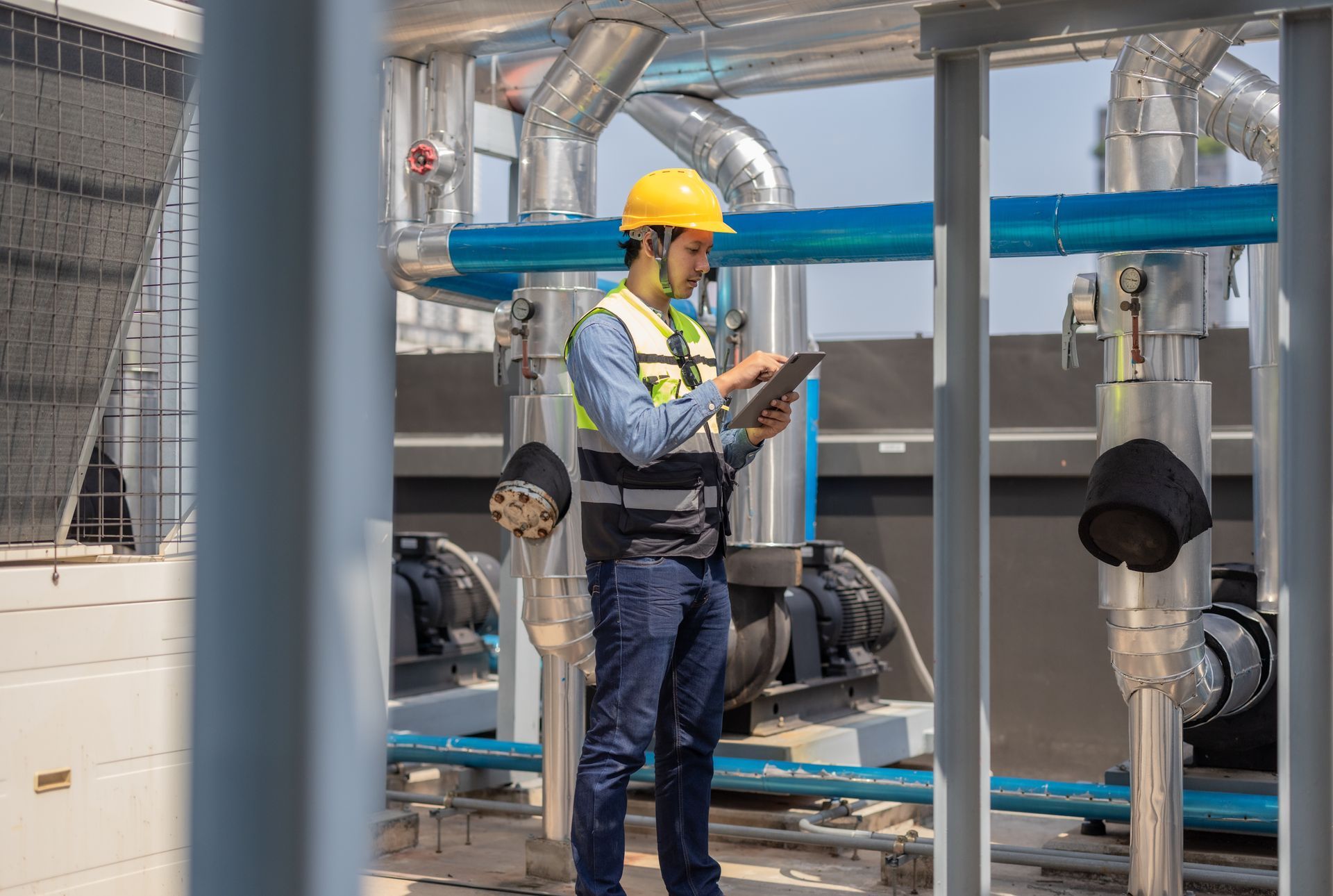 A man in a hard hat is using a tablet in a factory.