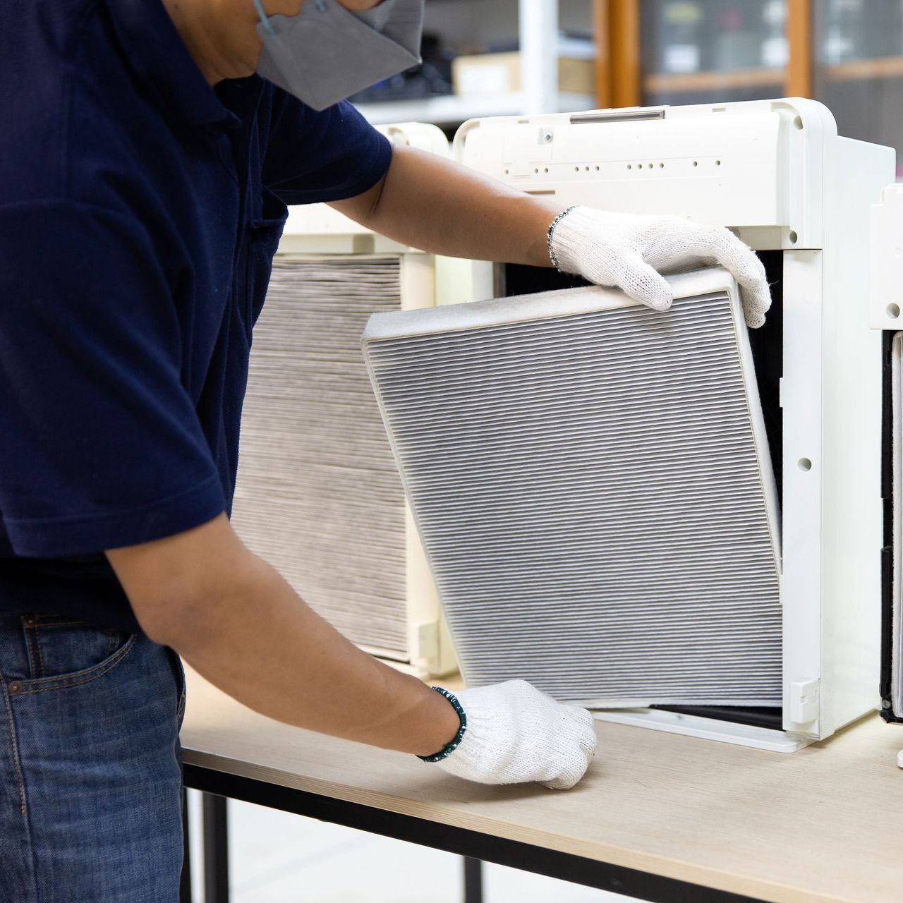 A man wearing a mask and gloves is changing a filter on an air purifier.