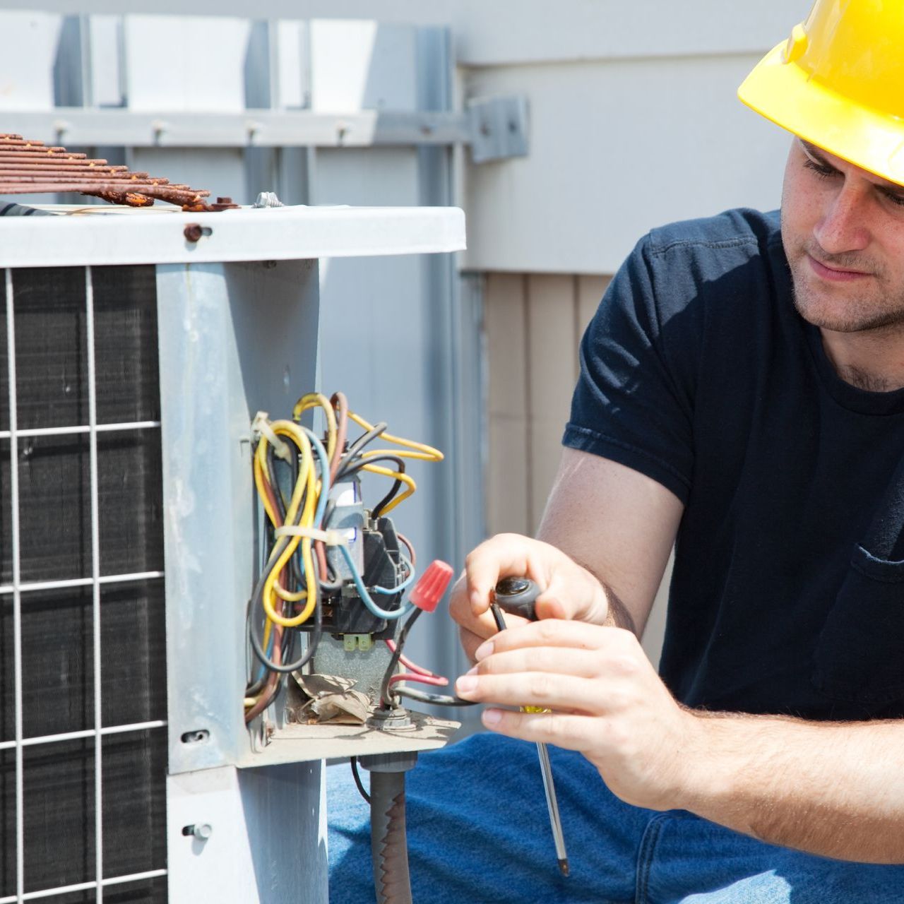 A man wearing a hard hat is working on an air conditioner.