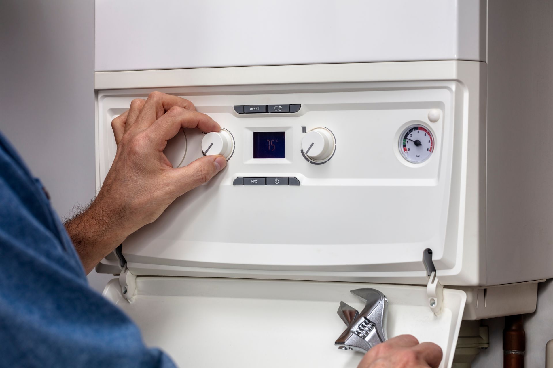 A man is adjusting a boiler and holding a wrench.