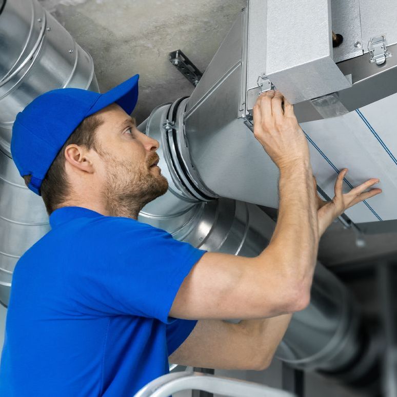 A man is working on a ventilation system in a building.