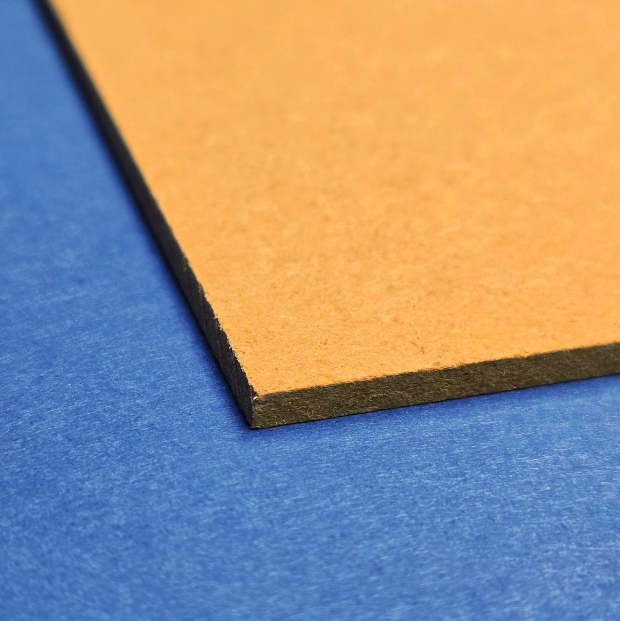 MDF board with smooth, brown finish shown at an angle against blue paper background, highlighting clean edge.