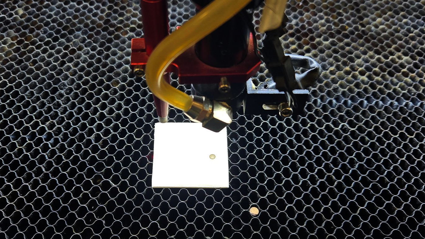 Laser nozzle firing test pulse onto tape on work bed to verify beam centering