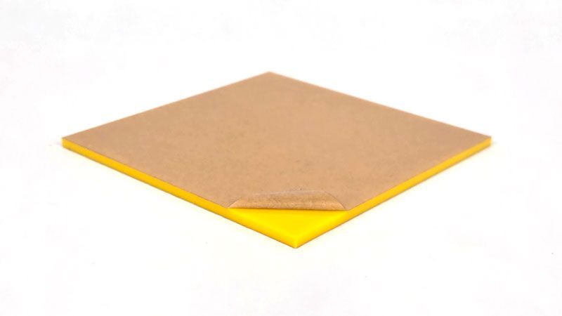 Yellow cast acrylic sheet with brown paper masking partially peeled back, showing thickness and layered edge.