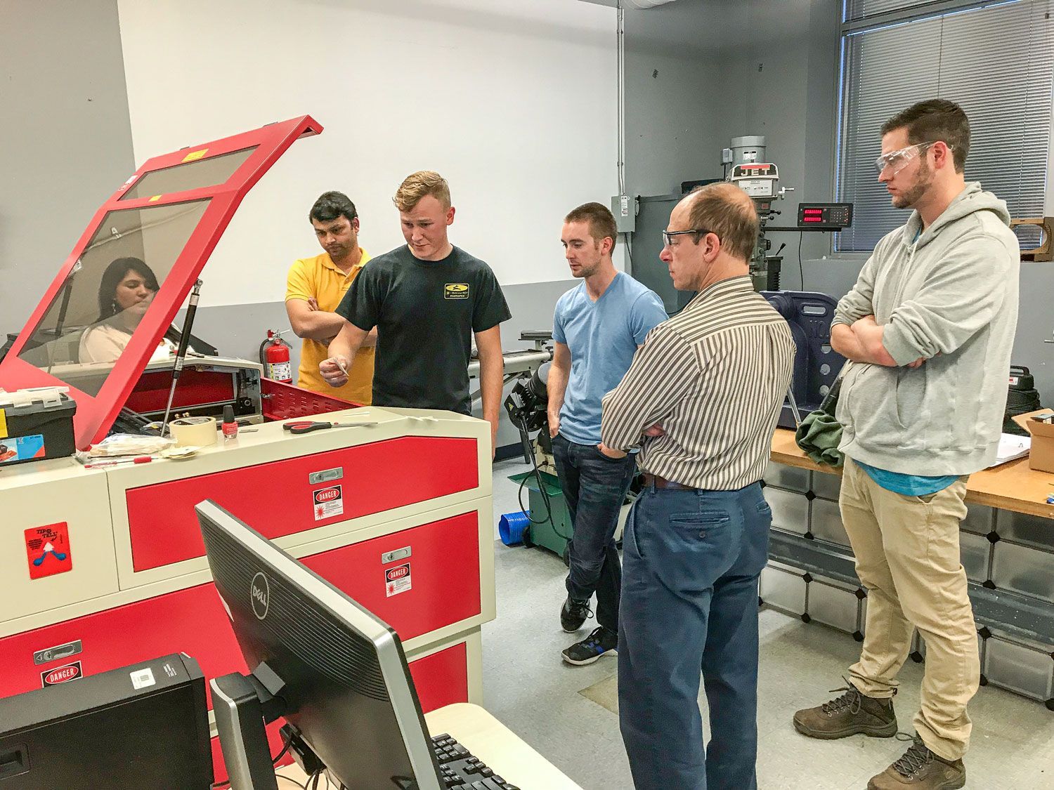 Group of people gathered around a red laser machine during training, with instructor demonstrating while others watch closely.