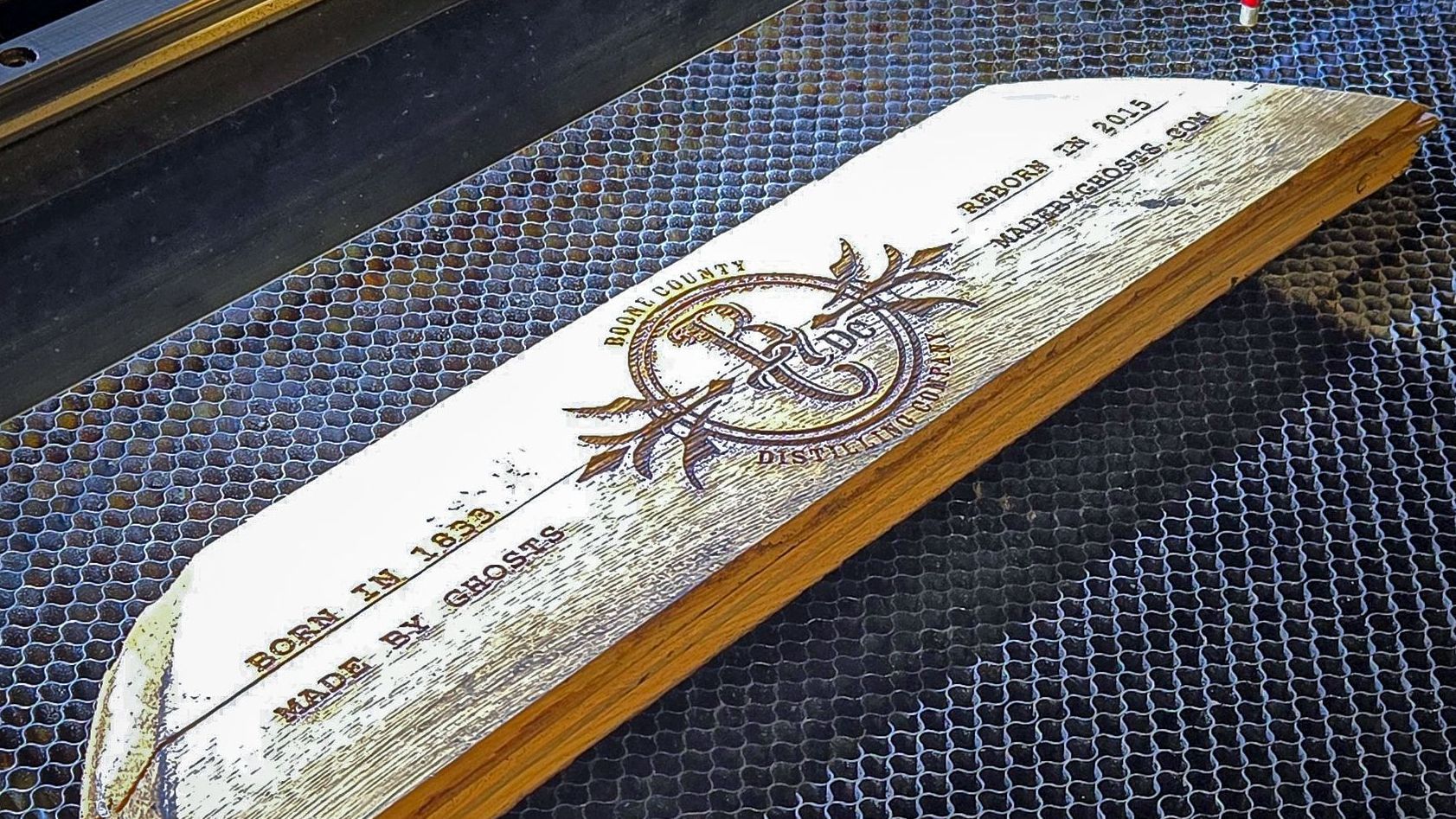 Laser-engraved whiskey barrel stave featuring Boone County Distilling Co. logo and rustic wood texture on honeycomb bed.