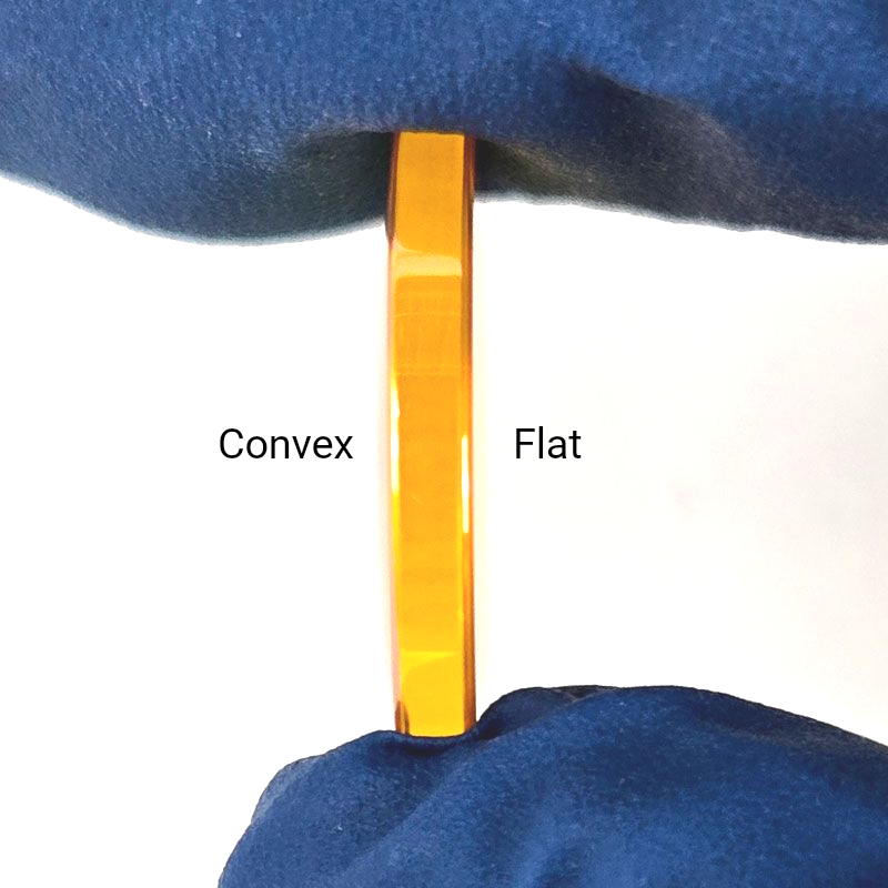 Gloved hands holding CO2 laser lens vertically to show edge profile and orientation
