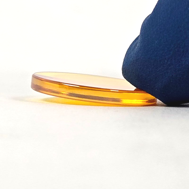 Close view of CO2 laser lens lying flat to compare convex and flat sides
