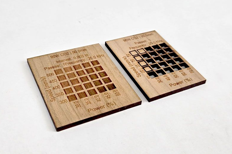 Two wooden material test cards on a white background, one engraved with test squares and settings labels, and the other cut through with square openings.
